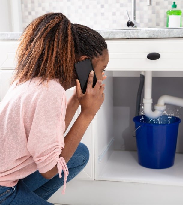 woman-calling-plumber-in-front-of-leaking-sink-pipe-picture-id1150345498-min